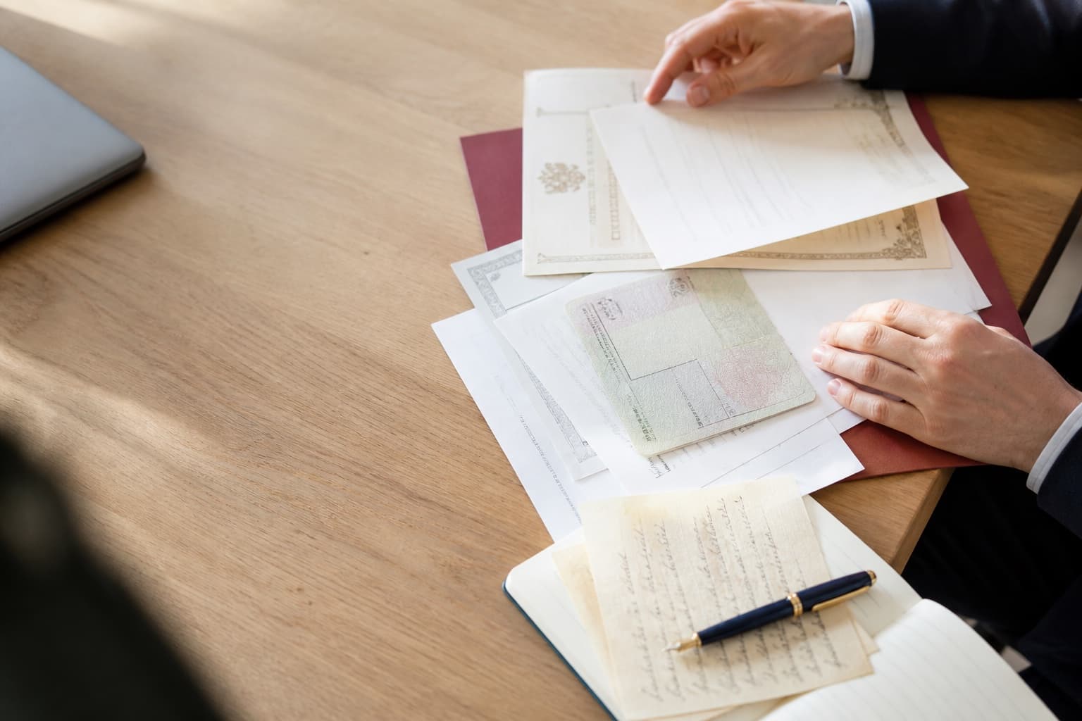 Des mains trient des feuilles et un livret ouvert à côté d’un carnet.