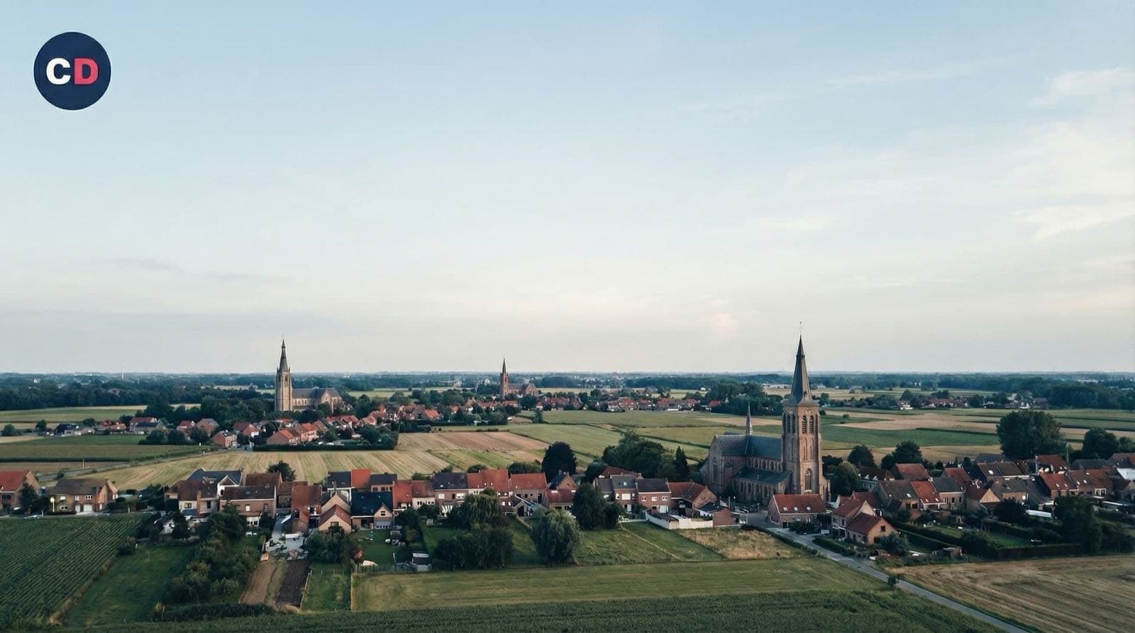 Vue sur des champs et une agglomération ponctuée de clochers.
