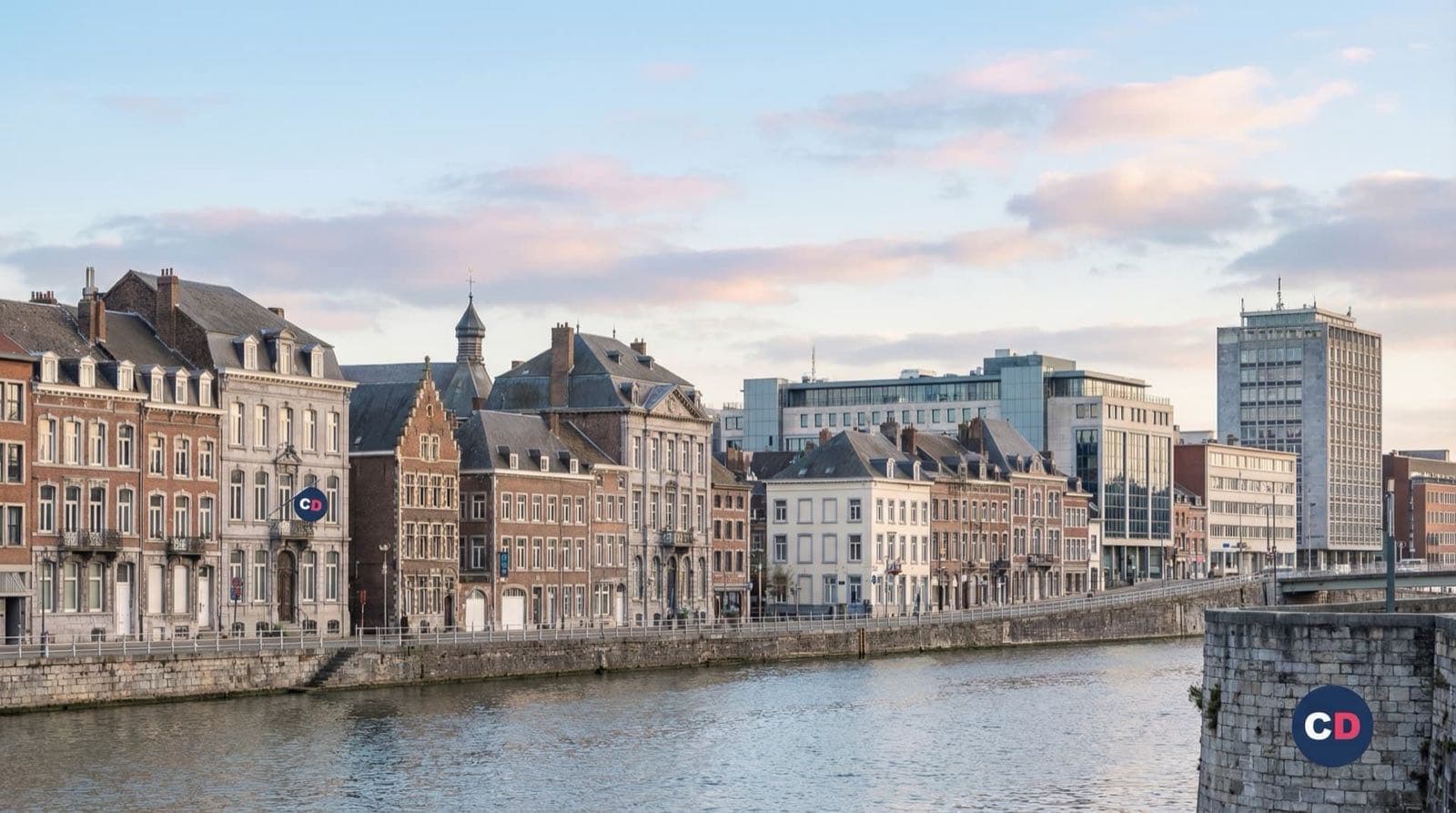 Des façades et des immeubles longent une rivière traversée par un pont.