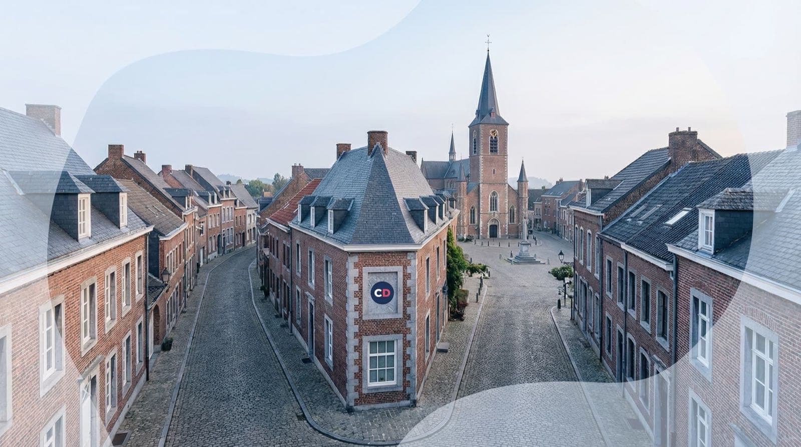 Vue sur des rues pavées bordées de maisons en briques et un clocher.